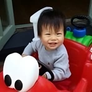 A young boy is smiling and driving a red toy car.