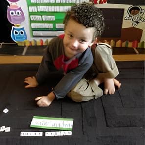 A young boy is sitting on a black carpet, playing with letters and toys.