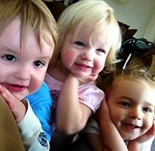 Three young children are sitting together, smiling for the camera.