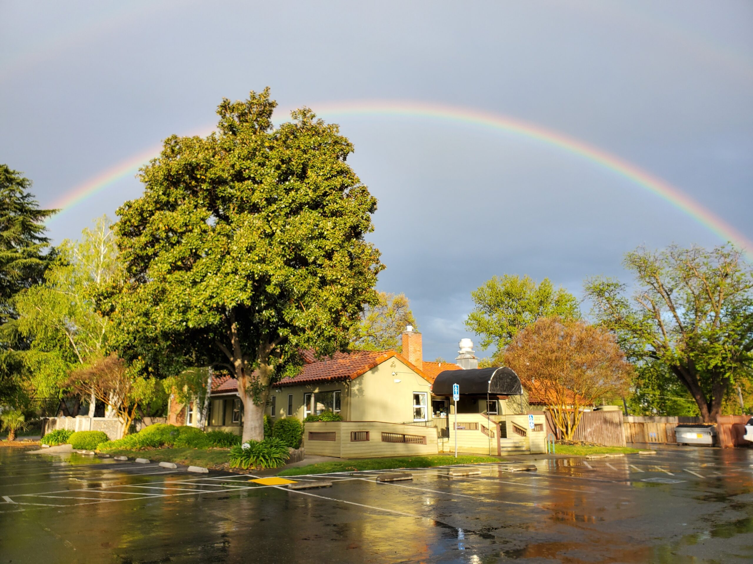 A rainbow arches over the building of Enchanted Play Preschool Center. The parking lot is wet from recent rain.